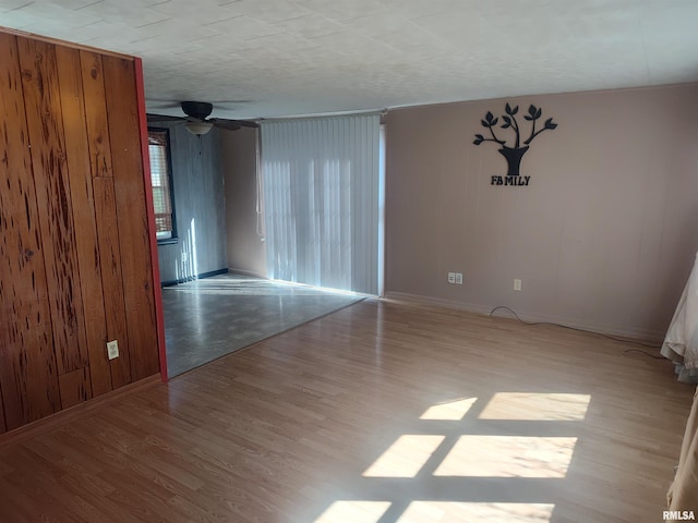 unfurnished room featuring ceiling fan, wood finished floors, wooden walls, and baseboards