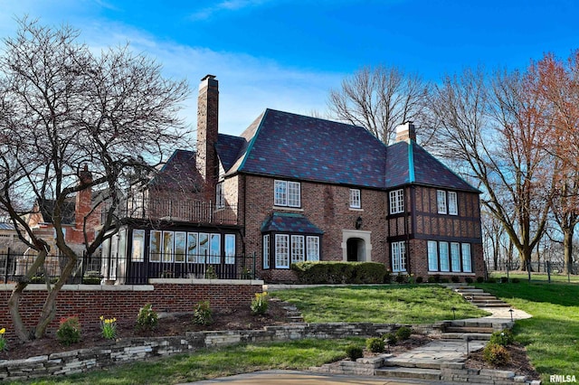 back of property with a high end roof, a chimney, brick siding, and a lawn