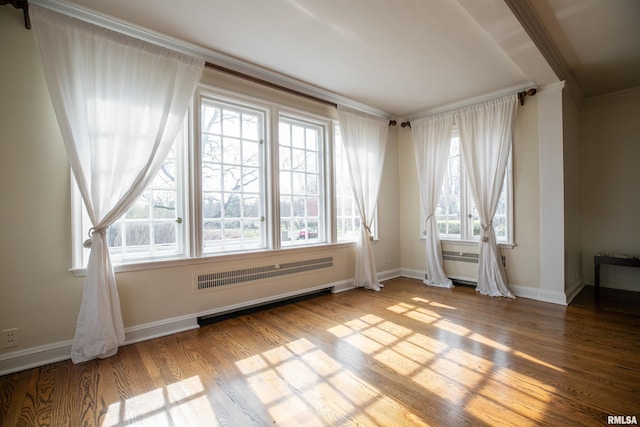 empty room featuring crown molding, wood finished floors, radiator heating unit, and baseboards