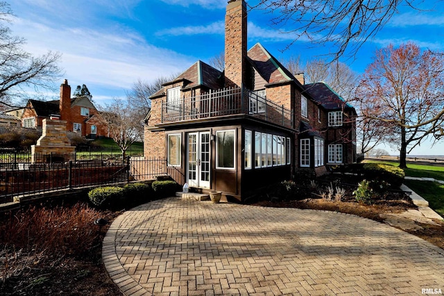 back of property with fence, a balcony, a chimney, and french doors