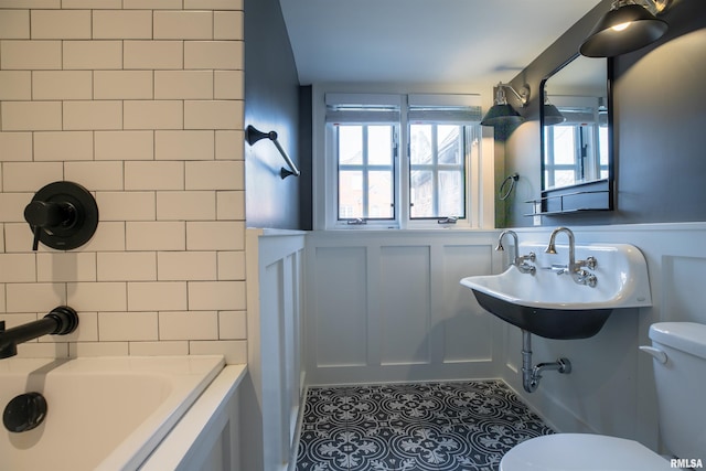 full bath with a tub, tile patterned floors, toilet, wainscoting, and a sink