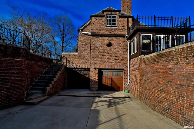 view of side of property featuring brick siding, an attached garage, stairs, and concrete driveway