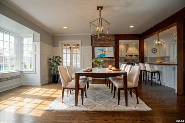 dining area with a decorative wall, a notable chandelier, wood finished floors, and crown molding