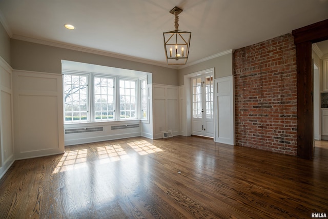 spare room with an inviting chandelier, crown molding, visible vents, a decorative wall, and wood finished floors