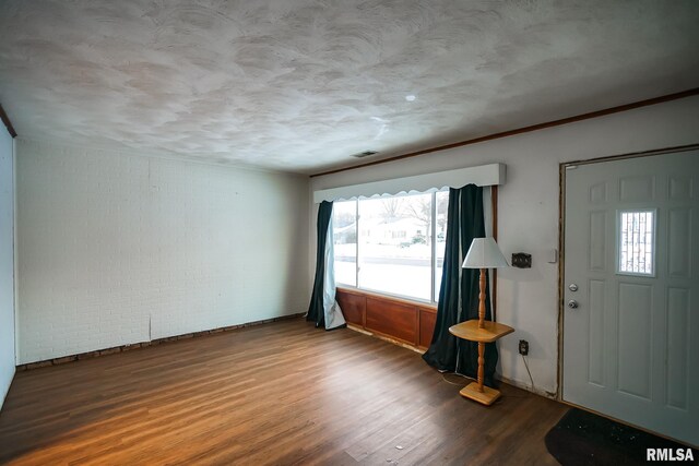foyer featuring a textured ceiling, wood finished floors, brick wall, and visible vents