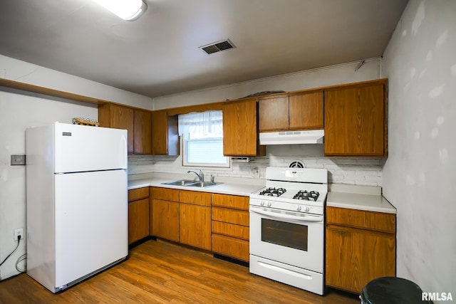 kitchen featuring white appliances, under cabinet range hood, a sink, light countertops, and decorative backsplash