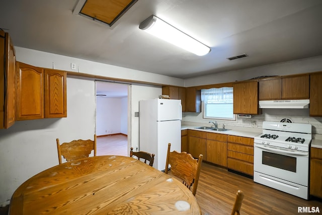 kitchen featuring a sink, white appliances, brown cabinetry, light countertops, and under cabinet range hood