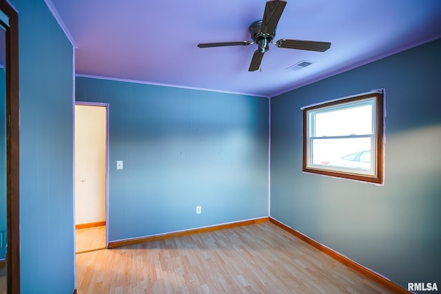 empty room with wood finished floors, visible vents, crown molding, baseboards, and ceiling fan