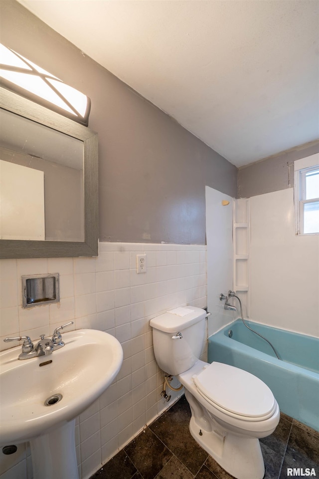 bathroom with a sink, tile walls, toilet, stone tile floors, and a wainscoted wall