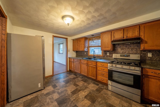 kitchen with a sink, brown cabinetry, under cabinet range hood, and stainless steel appliances