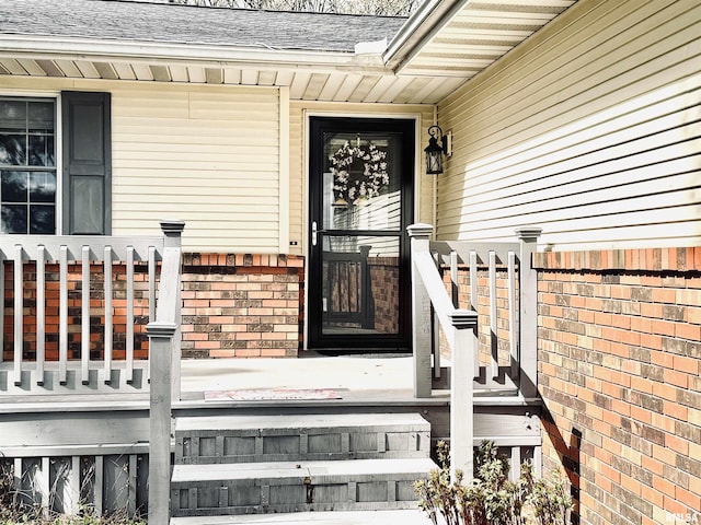 doorway to property with a shingled roof, brick siding, and covered porch