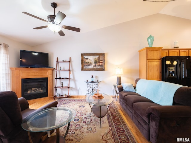 living room featuring a glass covered fireplace, vaulted ceiling, a ceiling fan, and wood finished floors