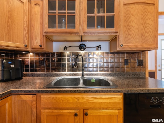 kitchen with glass insert cabinets, tasteful backsplash, black dishwasher, a sink, and dark countertops