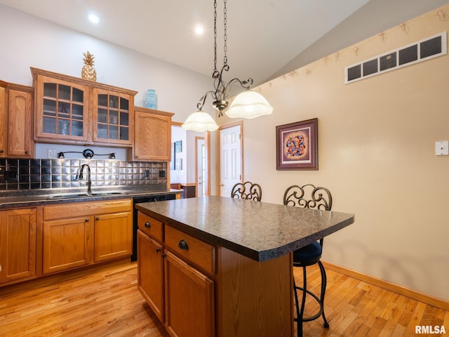 kitchen with visible vents, a sink, dark countertops, a kitchen breakfast bar, and vaulted ceiling