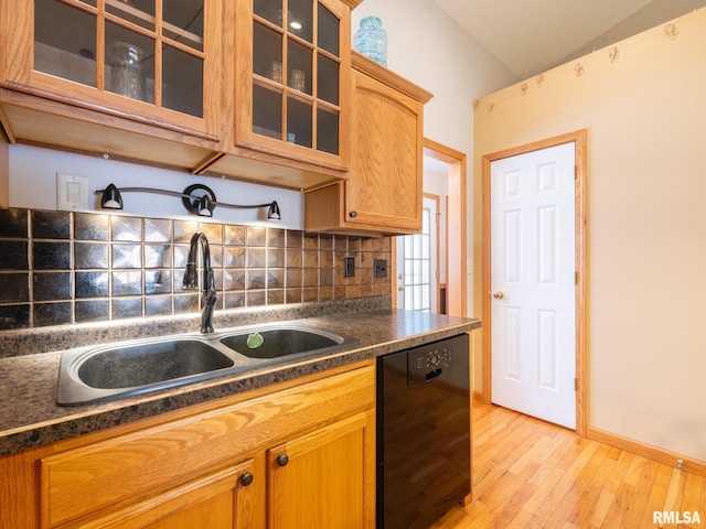 kitchen featuring glass insert cabinets, black dishwasher, dark countertops, decorative backsplash, and a sink