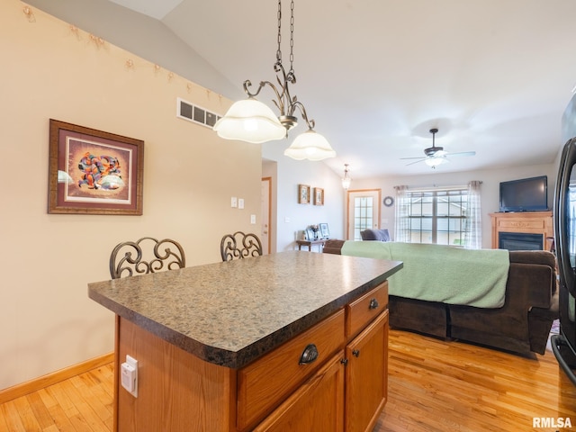 kitchen featuring open floor plan, a kitchen island, dark countertops, light wood-style floors, and visible vents