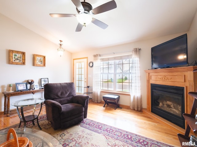 living area featuring a glass covered fireplace, lofted ceiling, baseboards, ceiling fan, and wood finished floors
