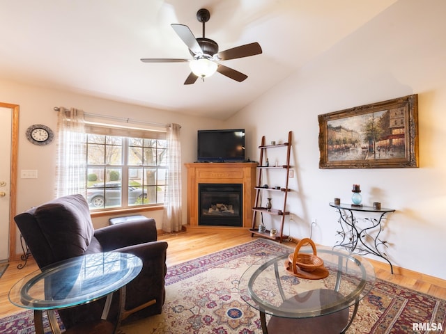 living area with wood finished floors, ceiling fan, a glass covered fireplace, and vaulted ceiling