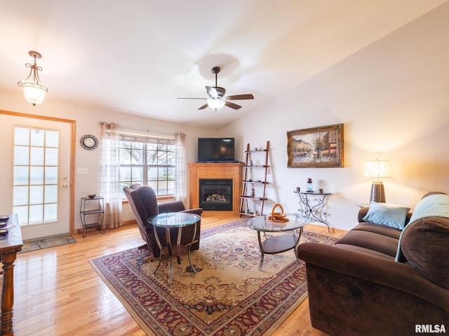 living area featuring a glass covered fireplace, lofted ceiling, light wood-style flooring, and ceiling fan