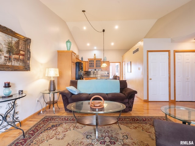 living room with light wood-style flooring, visible vents, baseboards, and lofted ceiling