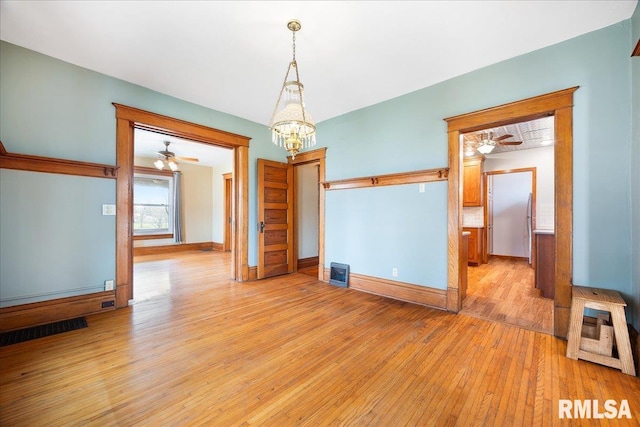empty room featuring visible vents, light wood-style flooring, baseboards, and ceiling fan with notable chandelier