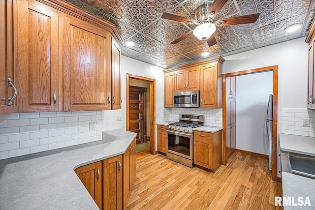 kitchen with a ceiling fan, appliances with stainless steel finishes, brown cabinets, backsplash, and an ornate ceiling