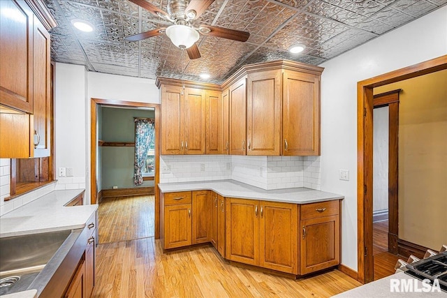kitchen with light wood-style flooring, backsplash, a ceiling fan, an ornate ceiling, and a sink