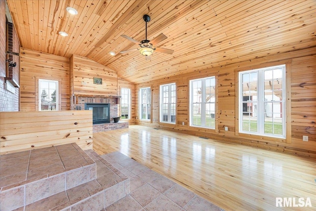 unfurnished living room with plenty of natural light, wooden walls, a brick fireplace, and lofted ceiling