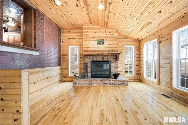 unfurnished living room featuring wooden walls, visible vents, wood-type flooring, and vaulted ceiling