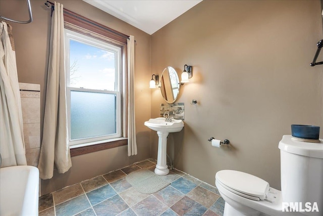 full bath with toilet, stone finish floor, and baseboards