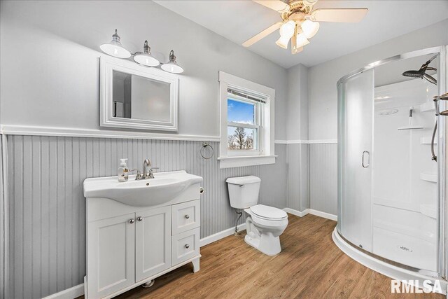full bath with toilet, a shower stall, vanity, wood finished floors, and a wainscoted wall