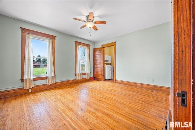 unfurnished room with washer / clothes dryer, light wood-type flooring, a ceiling fan, and baseboards