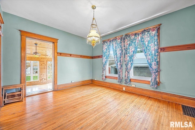 unfurnished dining area featuring baseboards, hardwood / wood-style floors, a notable chandelier, and visible vents