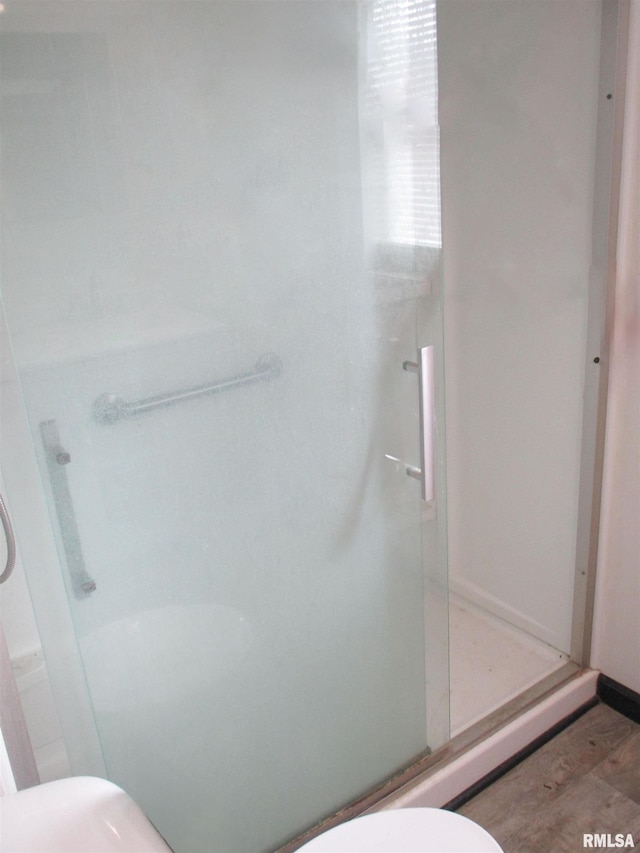 bathroom with wood finished floors, toilet, and a stall shower