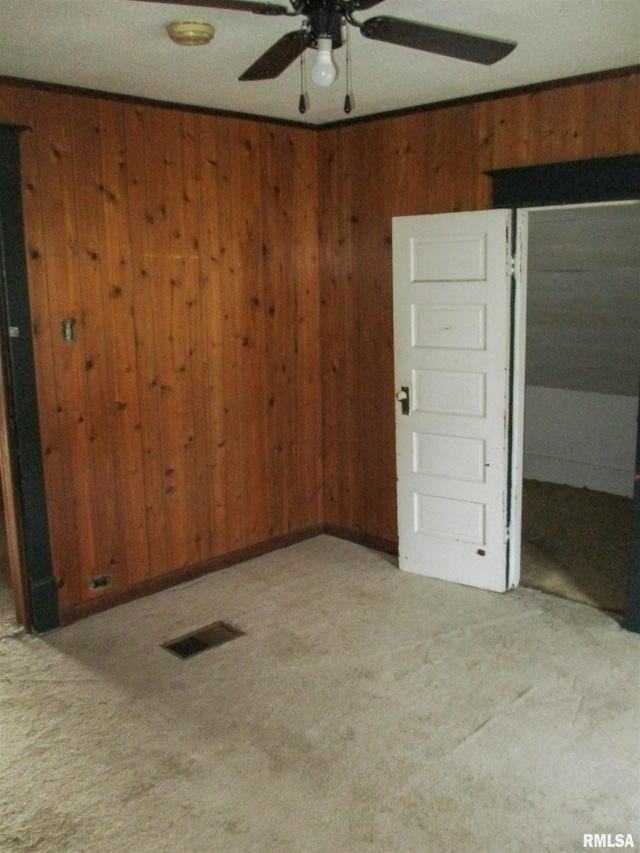 carpeted spare room featuring wooden walls, visible vents, and ceiling fan
