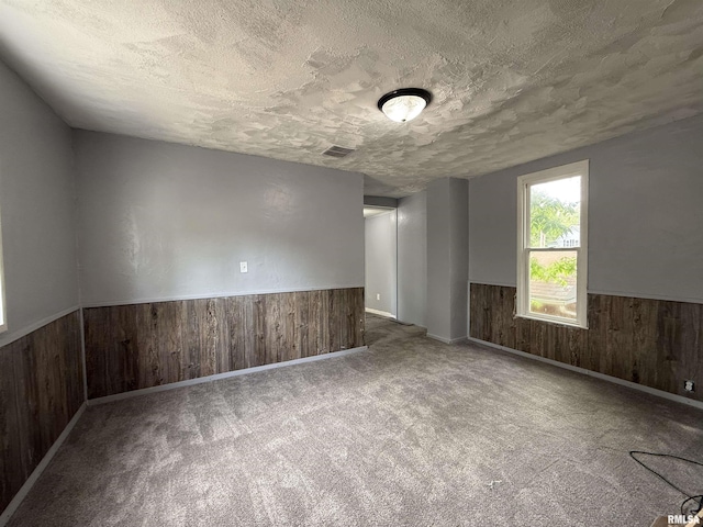 spare room featuring wooden walls, a textured ceiling, wainscoting, and carpet flooring
