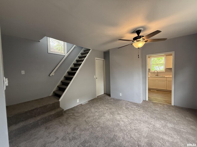 unfurnished living room featuring ceiling fan, stairs, carpet flooring, and a sink