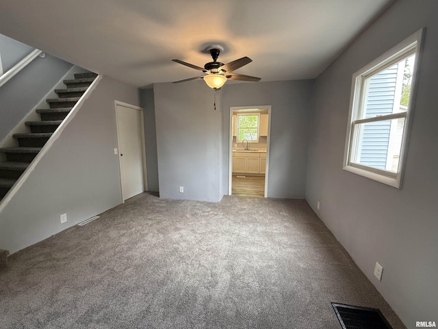 unfurnished living room with a sink, a ceiling fan, stairway, and carpet