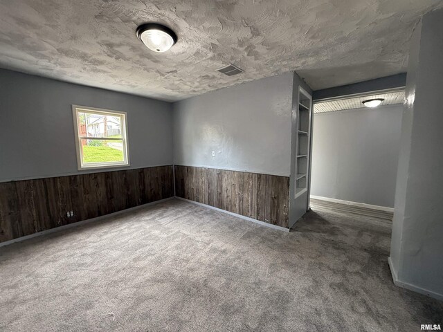 carpeted spare room featuring wooden walls and a wainscoted wall