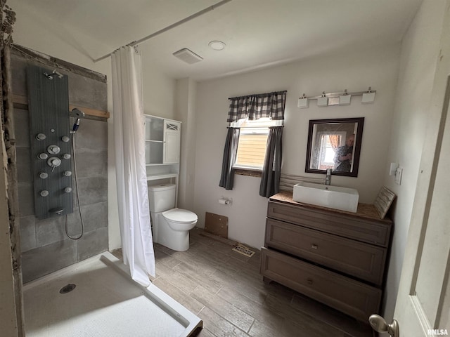 full bath featuring wood finished floors, vanity, toilet, and tiled shower