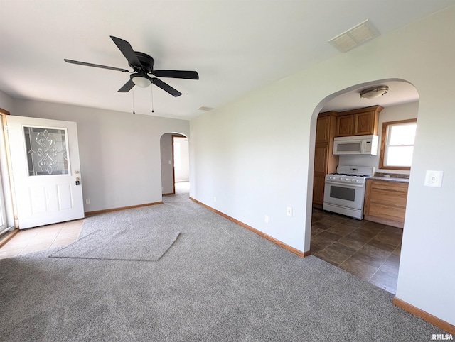 unfurnished living room with carpet, visible vents, arched walkways, baseboards, and ceiling fan