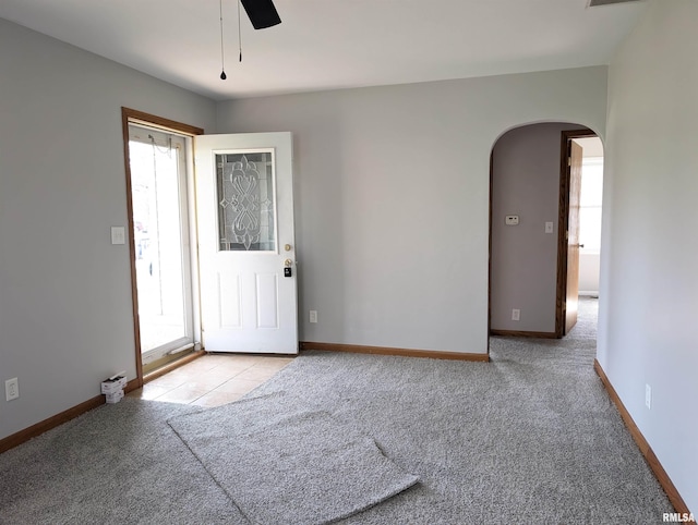 carpeted spare room featuring arched walkways, a wealth of natural light, a ceiling fan, and baseboards