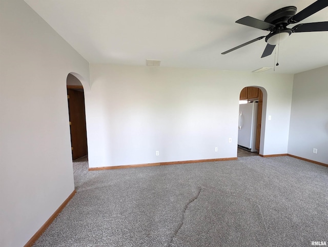spare room with arched walkways, carpet flooring, a ceiling fan, and baseboards