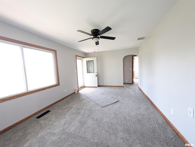 empty room featuring ceiling fan, visible vents, arched walkways, and carpet flooring