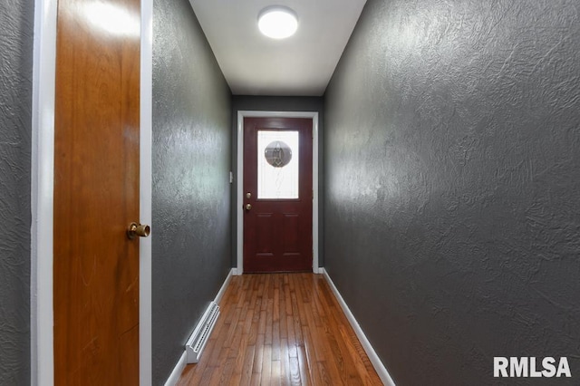 doorway to outside with wood-type flooring, a textured wall, visible vents, and baseboards