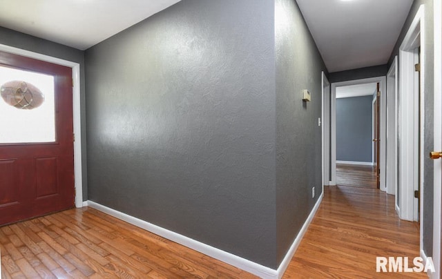 foyer entrance featuring baseboards, wood finished floors, and a textured wall