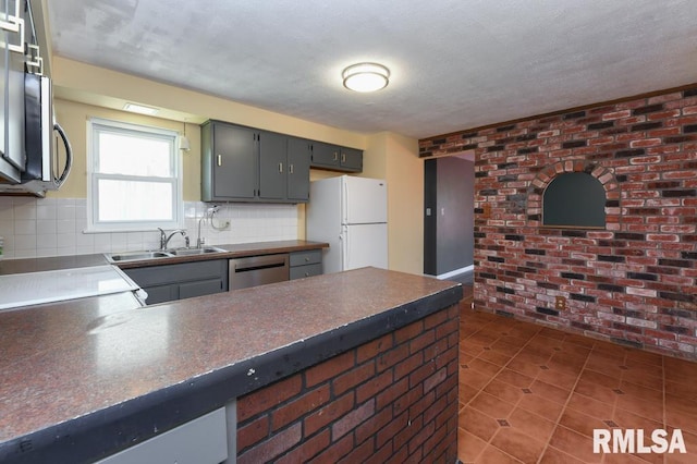 kitchen featuring dark countertops, a sink, dark tile patterned flooring, appliances with stainless steel finishes, and brick wall