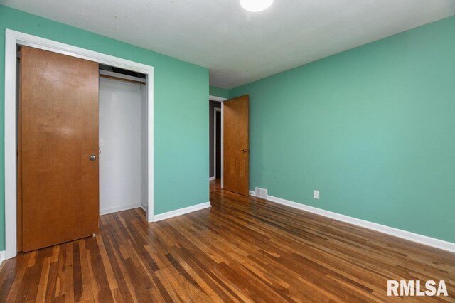 unfurnished bedroom featuring baseboards, wood finished floors, visible vents, and a closet