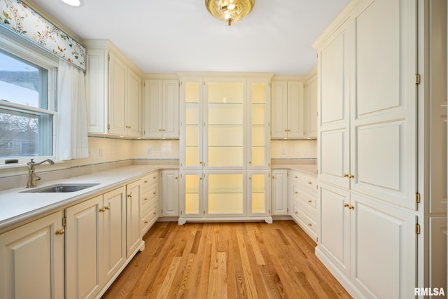 kitchen with light wood-style flooring, a sink, tasteful backsplash, glass insert cabinets, and light countertops