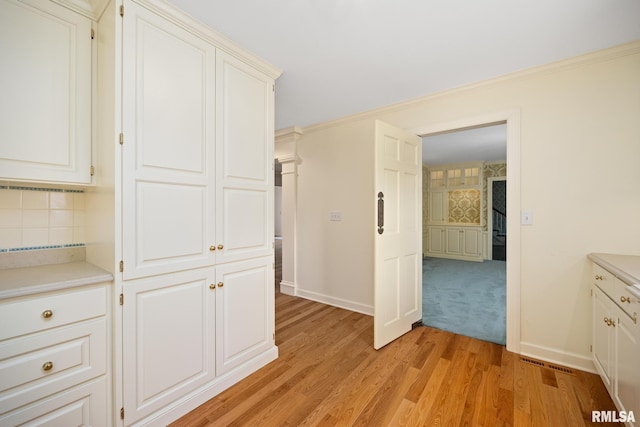 interior space with light wood-type flooring, baseboards, crown molding, and visible vents